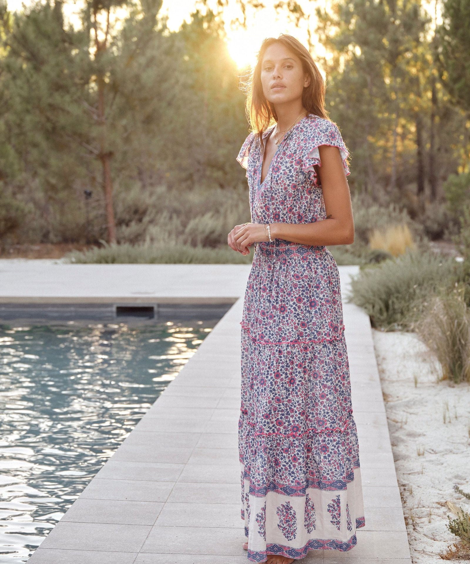 Woman in a Mabe Apparel Della resort maxi dress in blue and pink floral print with flutter sleeves.