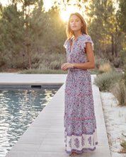 Woman in a Mabe Apparel Della resort maxi dress in blue and pink floral print with flutter sleeves.