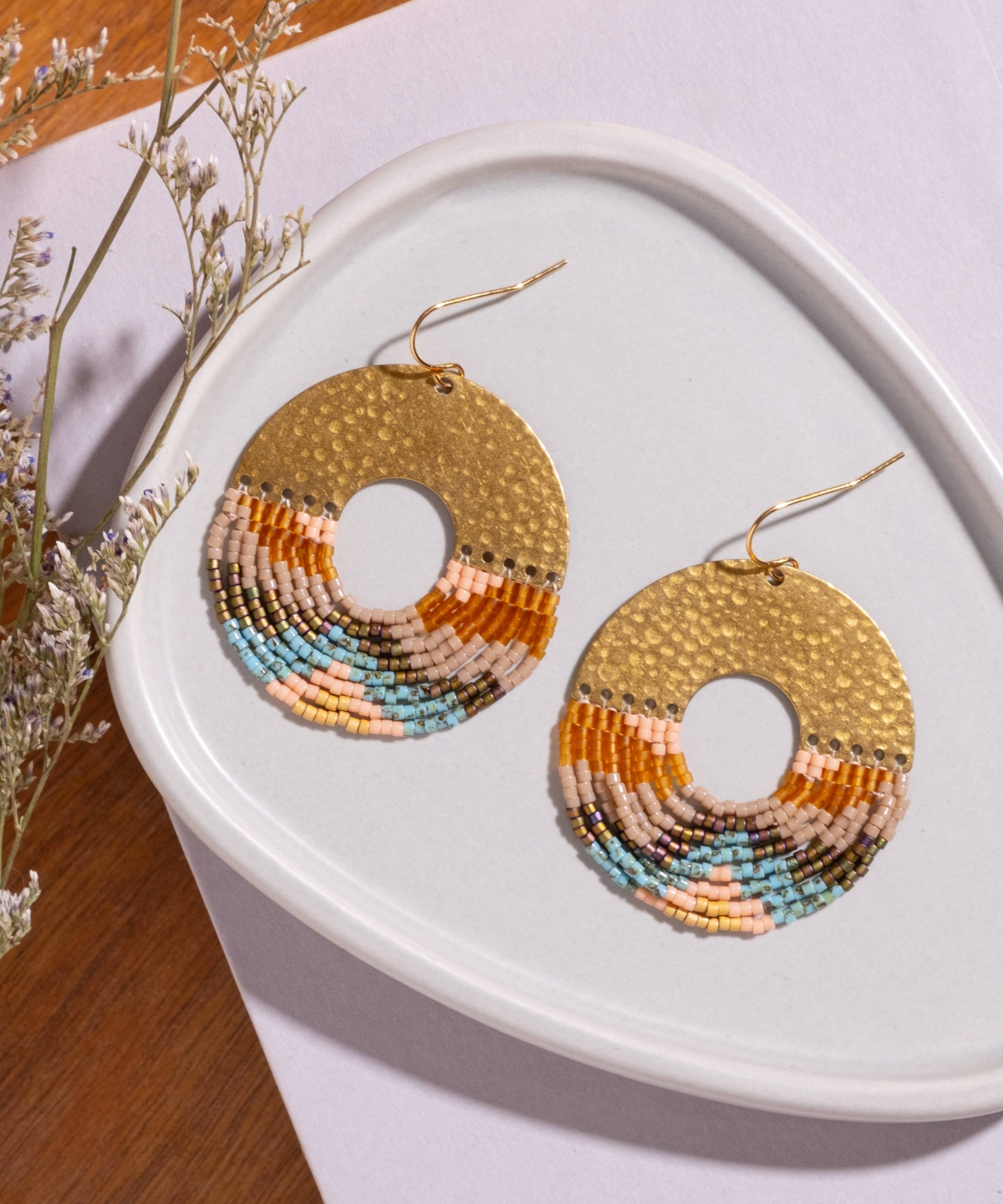 lose-up of Mayana Designs Earth Ombre Fringe Disk Earrings, highlighting the intricate beaded fringe in ombre colors and hammered brass arch.