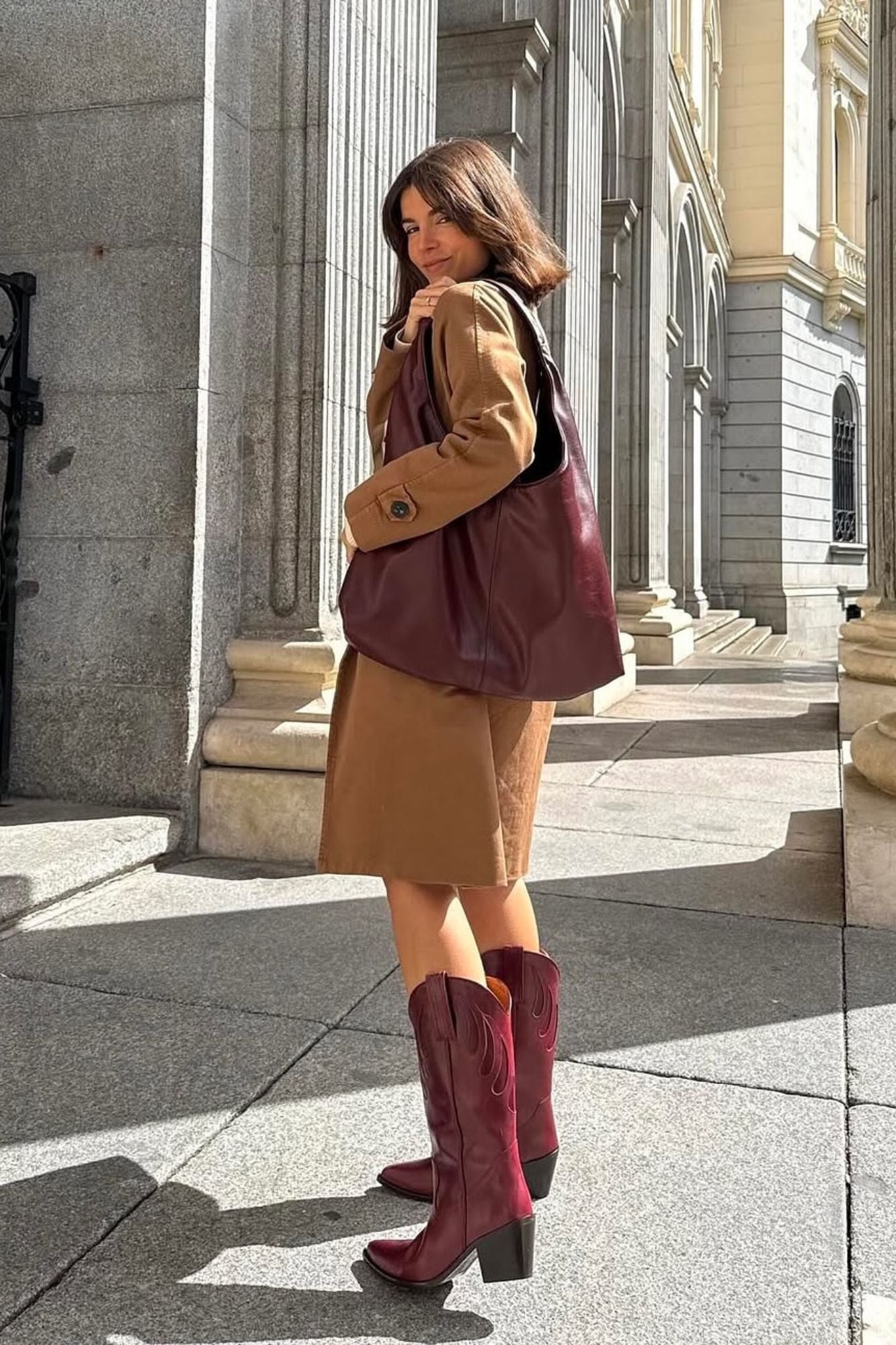 Woman wearing MICUIR Mestizo burgundy cowboy boots with a camel coat dress