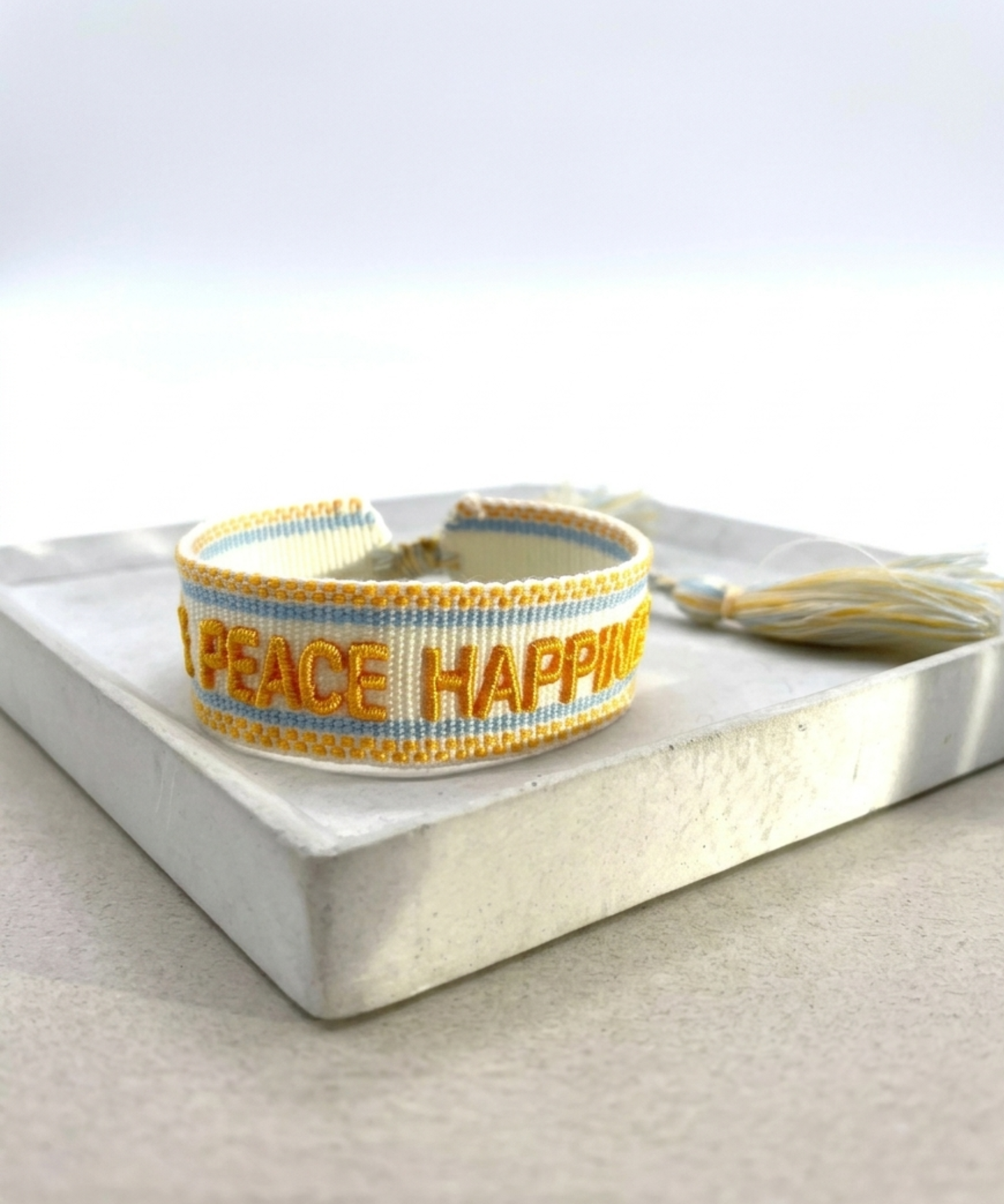 Cream woven Parsley & Pepper bracelet with mustard-yellow “LOVE PEACE HAPPINESS” embroidery, yellow and light blue borders – second view.
