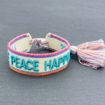 Close-up of adjustable woven turquoise friendship bracelet with embroidered “LOVE PEACE HAPPINESS” lettering and sliding knot tassel cords.