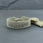 Close-up of adjustable sage eucalyptus woven bracelet with tone-on-tone embroidered “NAMASTE” lettering and sliding knot tassel cords.