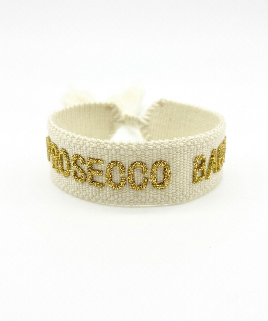 Close-up of adjustable ecru woven bracelet with gold embroidered “PROSECCO BABY” lettering and sliding knot tassel cords.