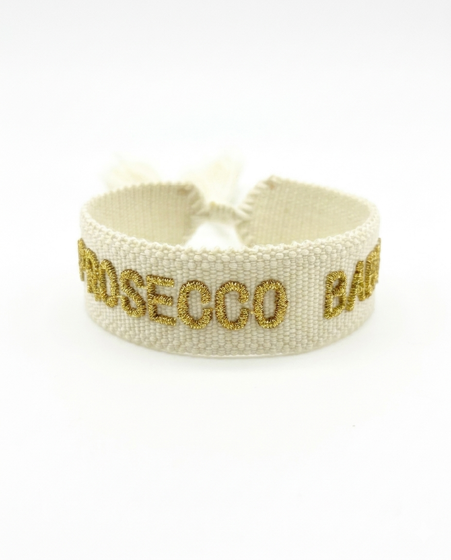 Close-up of adjustable ecru woven bracelet with gold embroidered “PROSECCO BABY” lettering and sliding knot tassel cords.