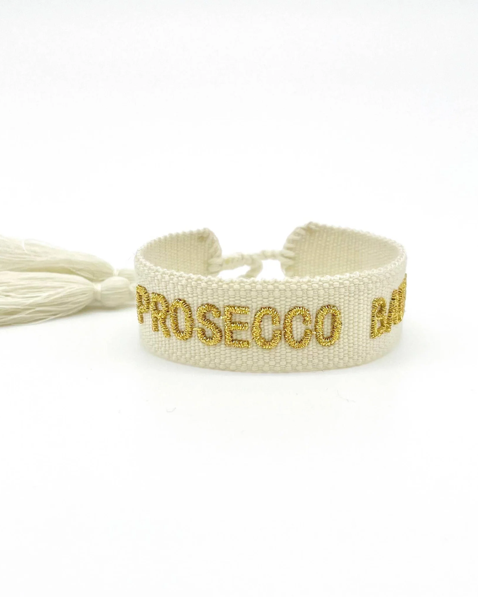 Close-up of adjustable ecru woven bracelet with gold embroidered “PROSECCO BABY” lettering and sliding knot tassel cords.