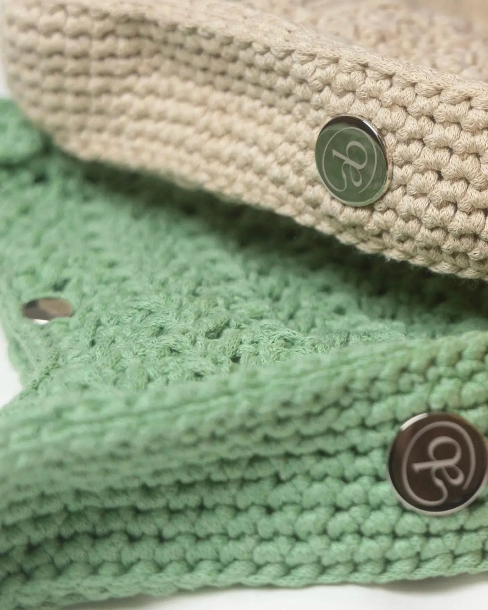 Close-up detail of Atelier Bagatelle's Riviera Lili crocheted bags in sage green and natural beige with logo