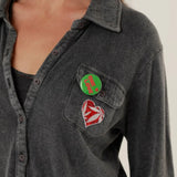 Close-up view of the Tess shirt front, showcasing the button closure, soft fabric texture, and removable green and red decorative badges.