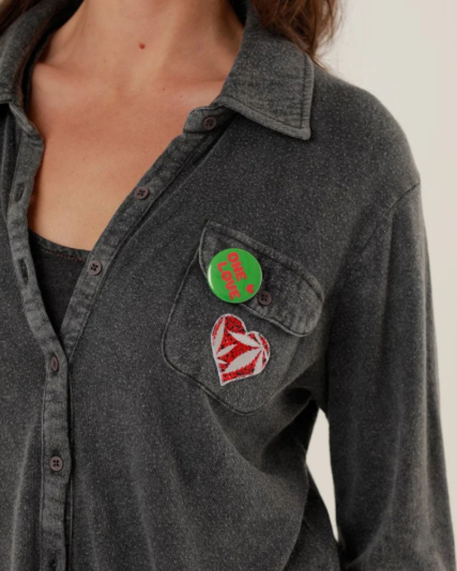 Close-up view of the Tess shirt front, showcasing the button closure, soft fabric texture, and removable green and red decorative badges.