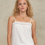 Close-up view of a model wearing a Mabe Apparel white embroidered cotton tank top with gold jewelry.