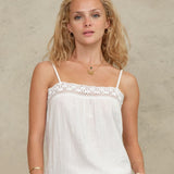 Close-up view of a model wearing a Mabe Apparel white embroidered cotton tank top with gold jewelry.