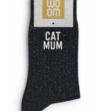 Classic black glitter message socks with a white jacquard CAT MUM inscription at the ankle, presented in their original Woom paper packaging.