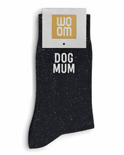 Black glitter message socks with a white jacquard DOG MUM inscription at the ankle, presented in their original Woom paper packaging.