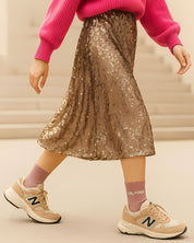 Close-up lifestyle shot of a model wearing the rose gold glitter message socks paired with a pleated gold skirt and casual sneakers.