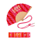 An opened summer folding fan with a dynamic red and pink striped pattern and LOVE IN THE AIR text, displayed alongside its matching pink shoulder cord and gift packaging.