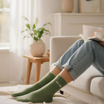 Cozy indoor lifestyle shot of a model relaxing on a couch, styling the almond green glitter message socks with casual home attire.