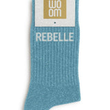 Vibrant turquoise glitter message socks with a white jacquard REBELLE inscription at the ankle, presented in their original Woom paper packaging.