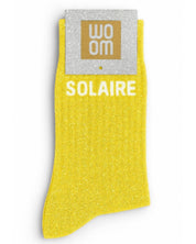 Vibrant yellow glitter message socks with a white jacquard SOLAIRE inscription at the ankle, presented in their original Woom paper packaging.