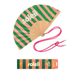 An opened summer folding fan with a dynamic green and pink striped pattern and white SOLEIL text, displayed alongside its matching pink shoulder cord and gift packaging.