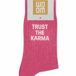 Vibrant pink glitter message socks with a white jacquard TRUST THE KARMA inscription at the ankle, presented in their original Woom paper packaging.