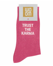 Vibrant pink glitter message socks with a white jacquard TRUST THE KARMA inscription at the ankle, presented in their original Woom paper packaging.