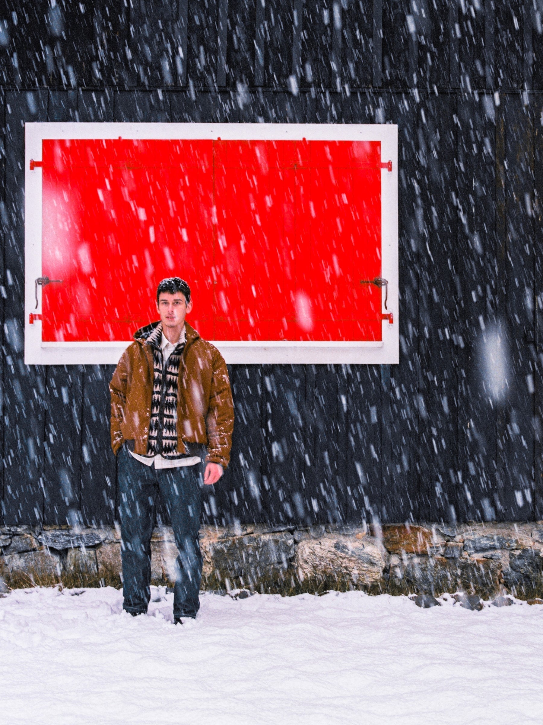 A man standing in the snow wearing Rust Hooded Duck Jacket by Menswear Label Crest.