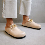 Close-up of the ALOHAS nude clogs worn with cream trousers, highlighting the gold chain detail.