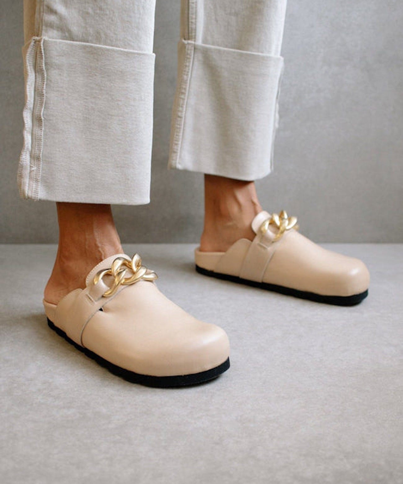 Close-up of the ALOHAS nude clogs worn with cream trousers, highlighting the gold chain detail.