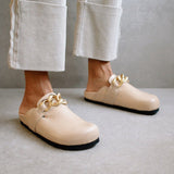 Close-up of the ALOHAS nude clogs worn with cream trousers, highlighting the gold chain detail.