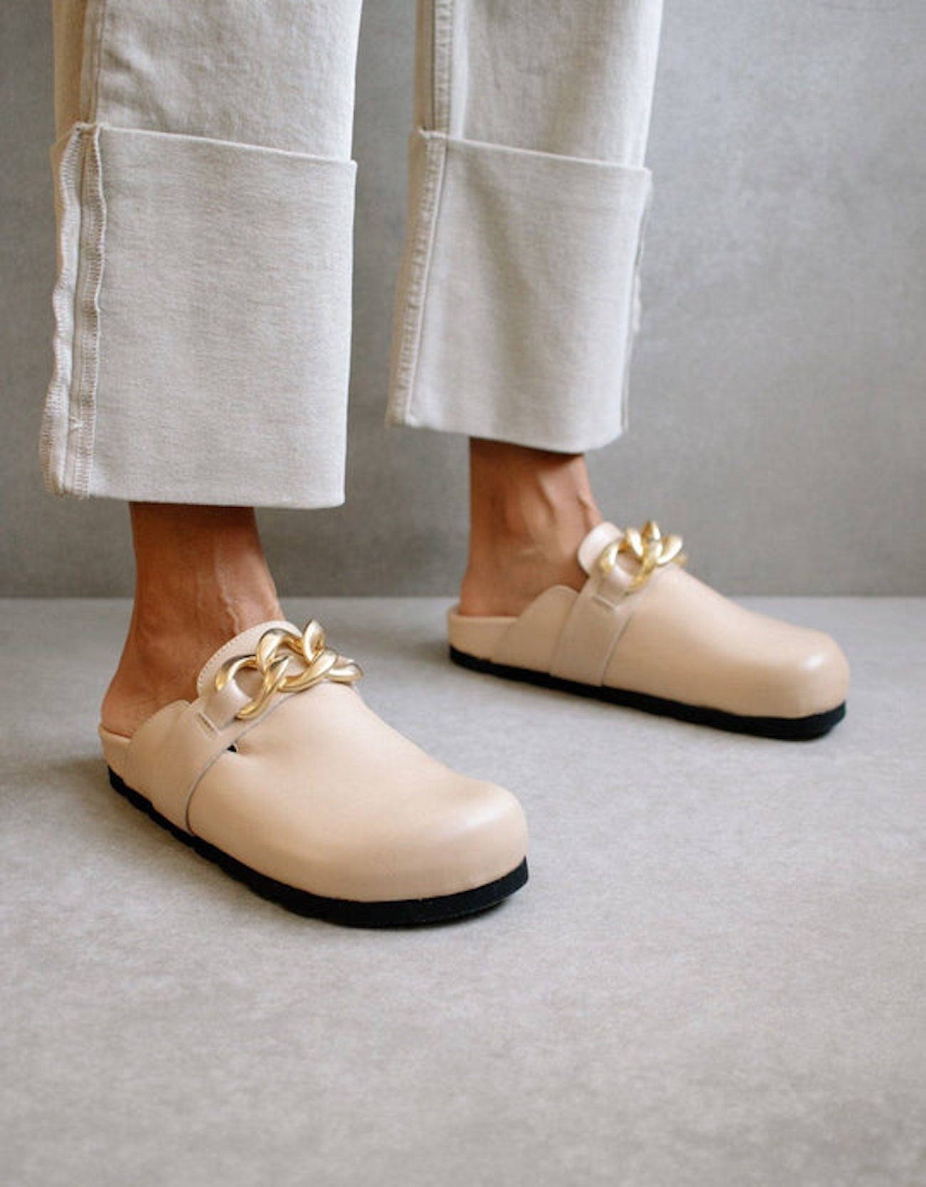 Close-up of the ALOHAS nude clogs worn with cream trousers, highlighting the gold chain detail.