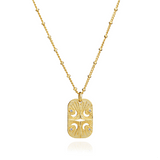 Azuni Astral ID Tag necklace, a gold rectangular tag engraved with a moon and stars on a beaded chain.
