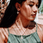 Model wearing the Azuni Astral ID Tag pendant layered with a fine necklace over a green top.