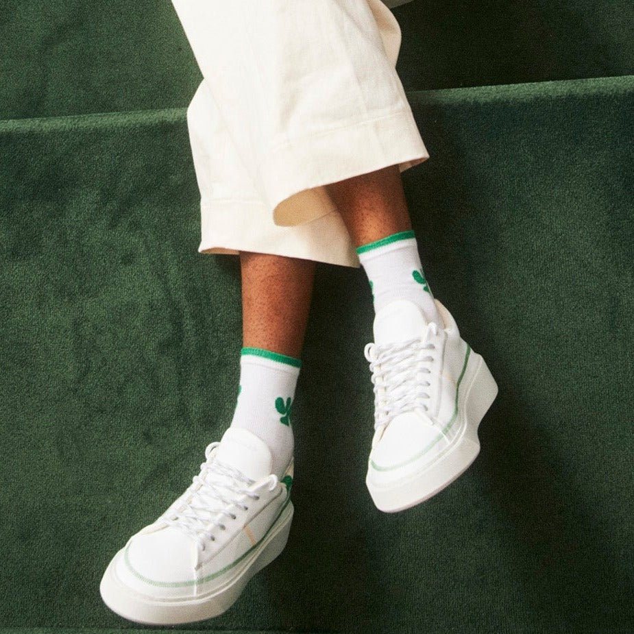A person sitting on a tennis court wearing Bonamaso ecological sneakers and the brands signature socks in green
