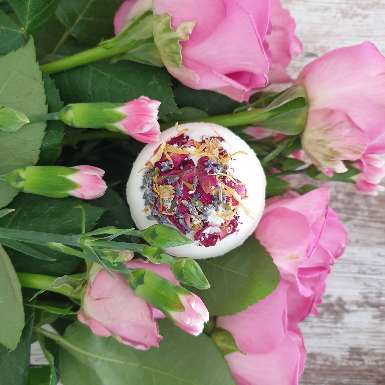 Floral Secret Bath Bomb has a sweet smell thanks to geranium and lavender, photographed with pink flowers.