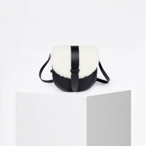 Craie Studio Mini Louna saddle bag with a cream lamb-fur body and black leather flap and strap, on a plinth.