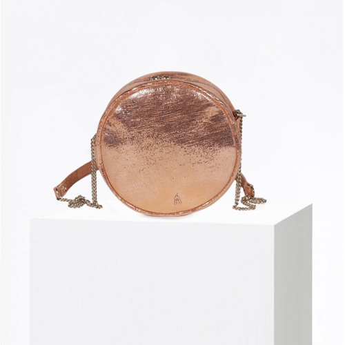 Craie Studio EYES round crossbody bag in rose-gold metallic leather with a leather-and-chain strap, on a plinth.