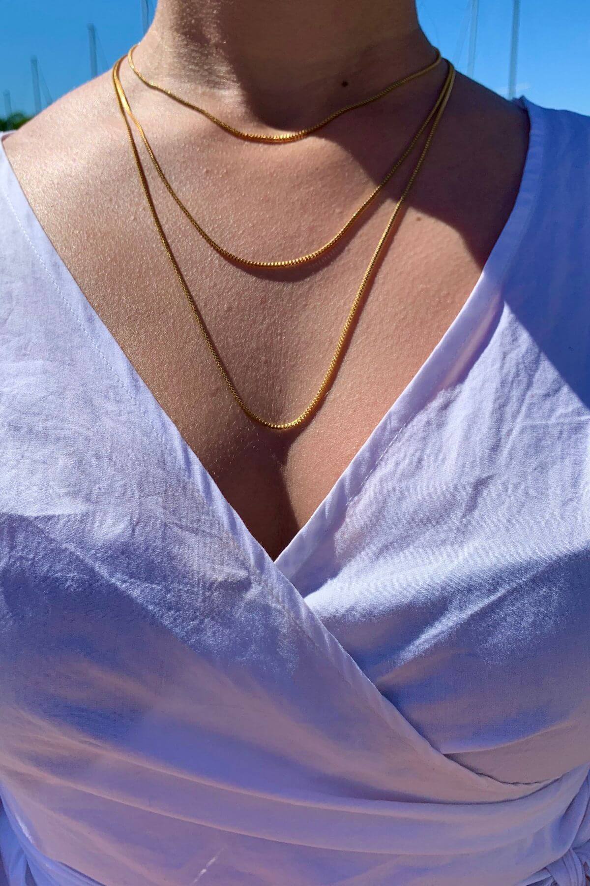 Crystal Haze gold-plated box chain necklace worn with a white top, outdoor lifestyle shot