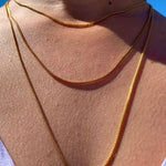 Crystal Haze gold-plated box chain necklace worn layered against a blue sky backdrop