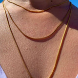 Crystal Haze gold-plated box chain necklace worn layered against a blue sky backdrop
