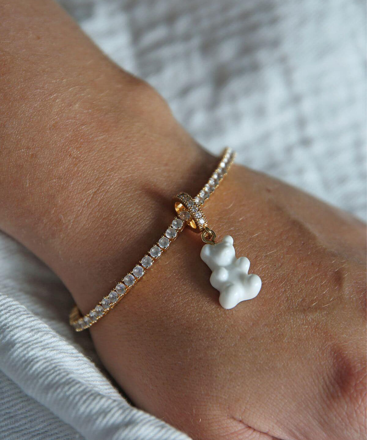 Close-up of the Crystal Haze white Nostalgia Bear charm on a fine gold chain at the wrist.