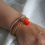 Crystal Haze red Nostalgia Bear charm stacked with beaded and gold-chain bracelets on the wrist.