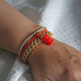 Crystal Haze red Nostalgia Bear charm stacked with beaded and gold-chain bracelets on the wrist.