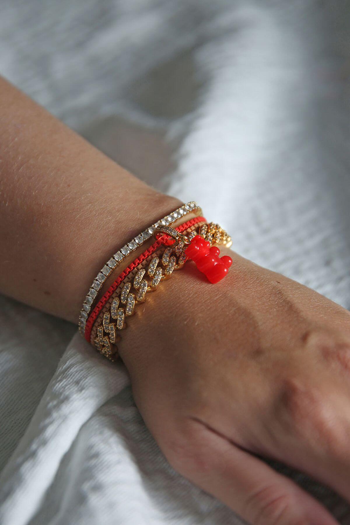 Crystal Haze red Nostalgia Bear charm stacked with beaded and gold-chain bracelets on the wrist.
