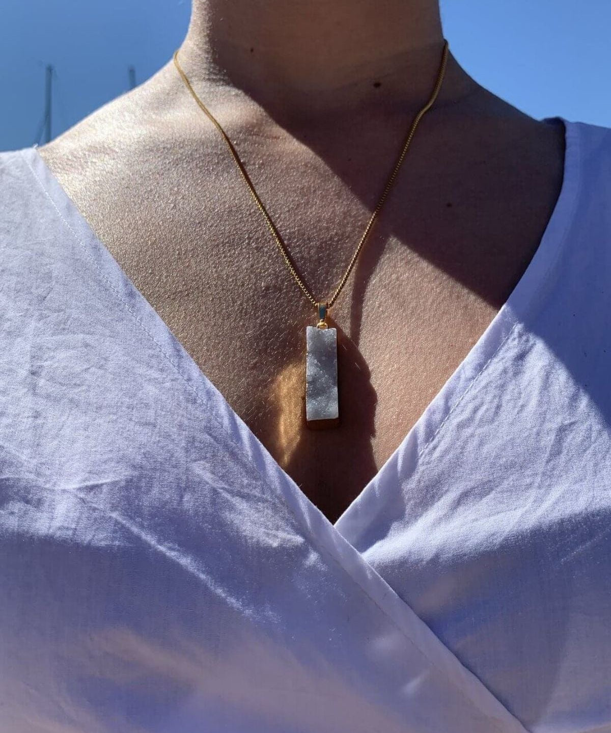 Crystal Haze grey agate pendant worn on a fine gold chain, outdoor lifestyle shot with a white top.