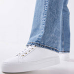 Woman wearing the Nubikk Jolie white leather sneakers with blue jeans, street-style shot.