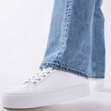 Woman wearing the Nubikk Jolie white leather sneakers with blue jeans, street-style shot.