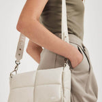 NUBIKK beige May leather bag worn crossbody with an olive top and grey trousers