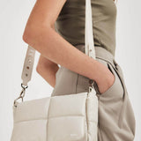 NUBIKK beige May leather bag worn crossbody with an olive top and grey trousers